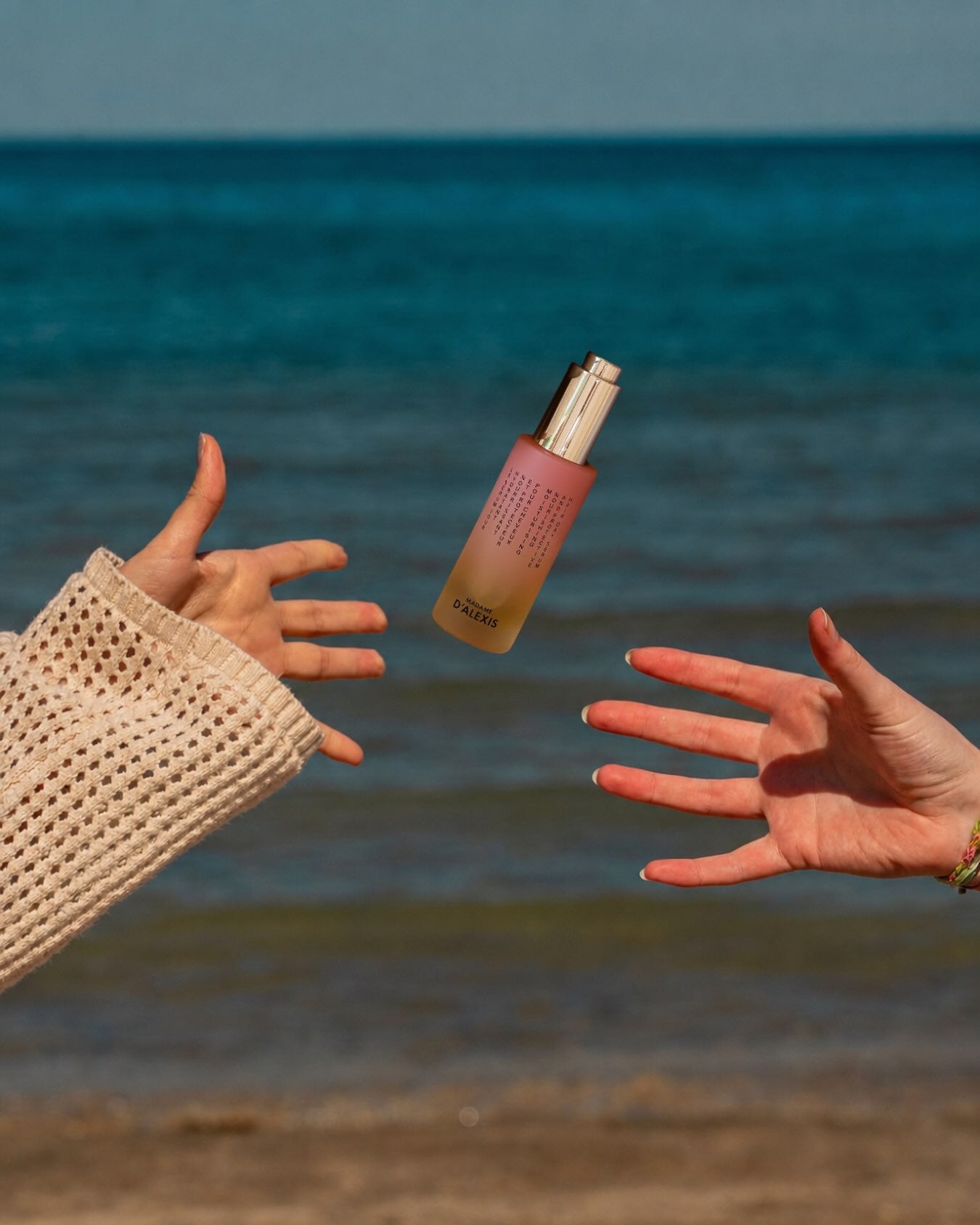 Deux mains se tendent un flacon de sérum Madame d’Alexis, avec la mer en arrière-plan